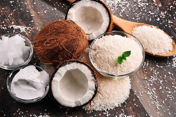 Organic Shredded Coconuts in the small bowl and in the wooden spoon on the wooden table with half coconuts by Anna and Sarah