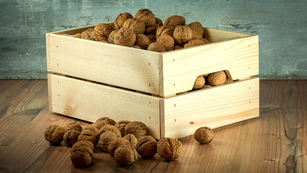 Lots of Walnuts in Shell in a wooden basket on the wooden ground with blue wall background by Anna and Sarah